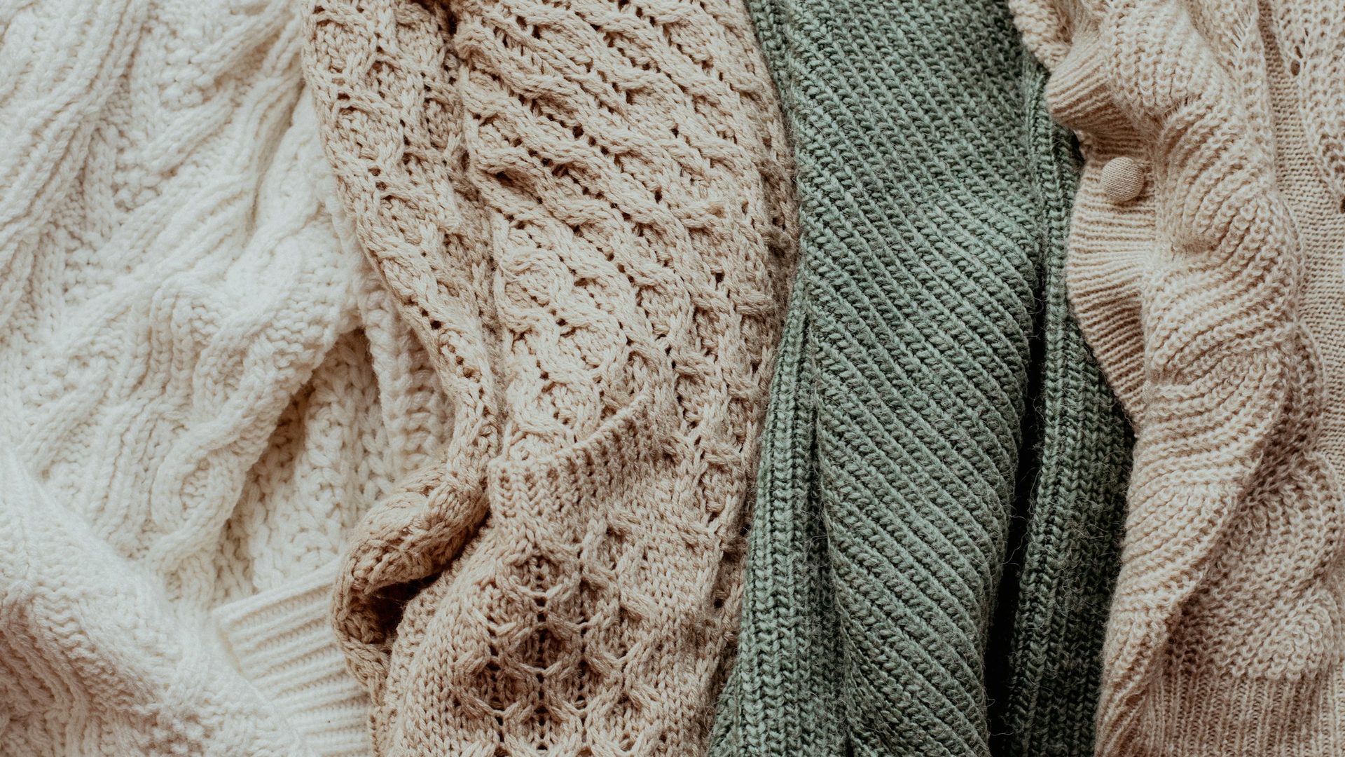 Maglioni in maglia di lana color panna, beige e verde salvia accostati uno accanto all'altro
